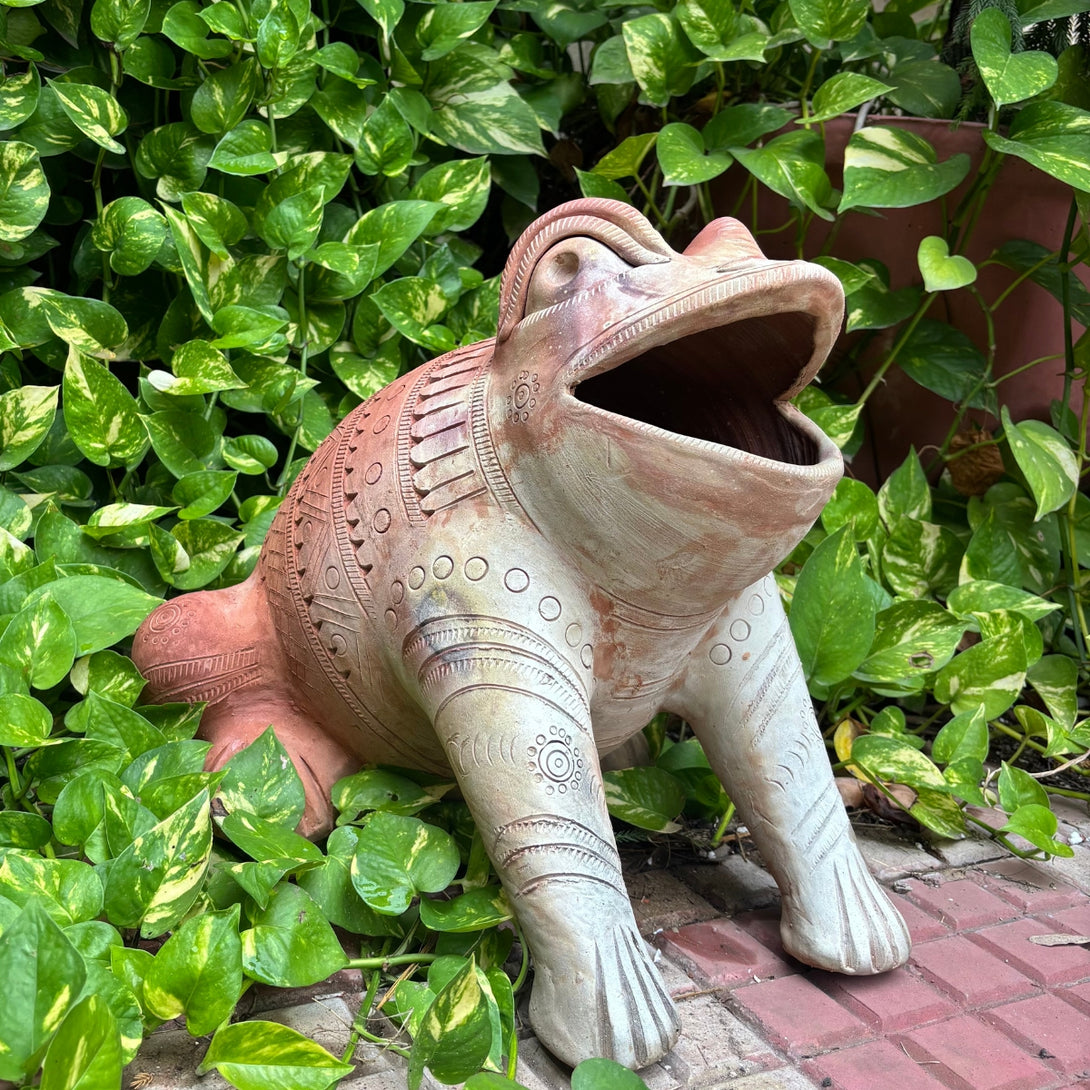 Decorative frog statue with open mouth in a garden setting