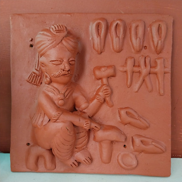 A terracotta tile featuring a sculpted cobbler with various tools, set against a plain background.